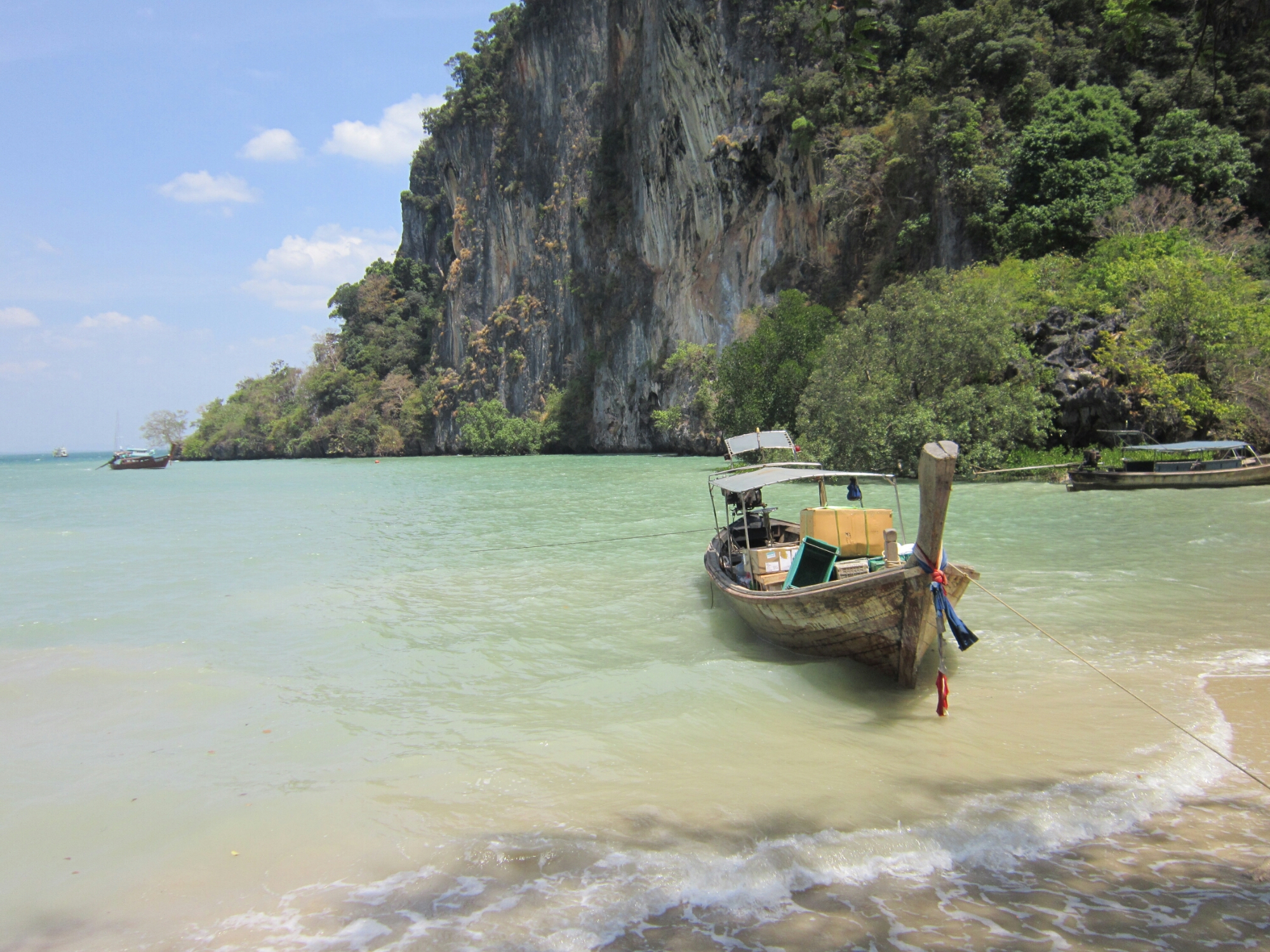 A boat moored at the Tonsai beach whilst the tide is in. Limestone cliffs rise up in the background. 