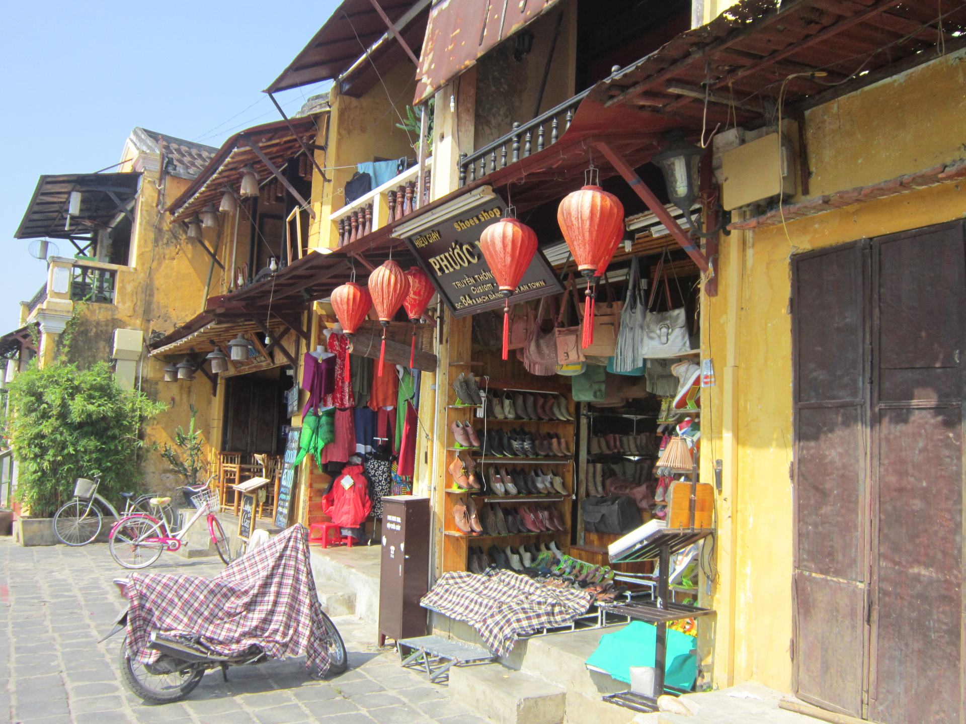 A shop front in Hội An, Vietnam. There are several red Chinese lanterns hanging over the entrance. 
